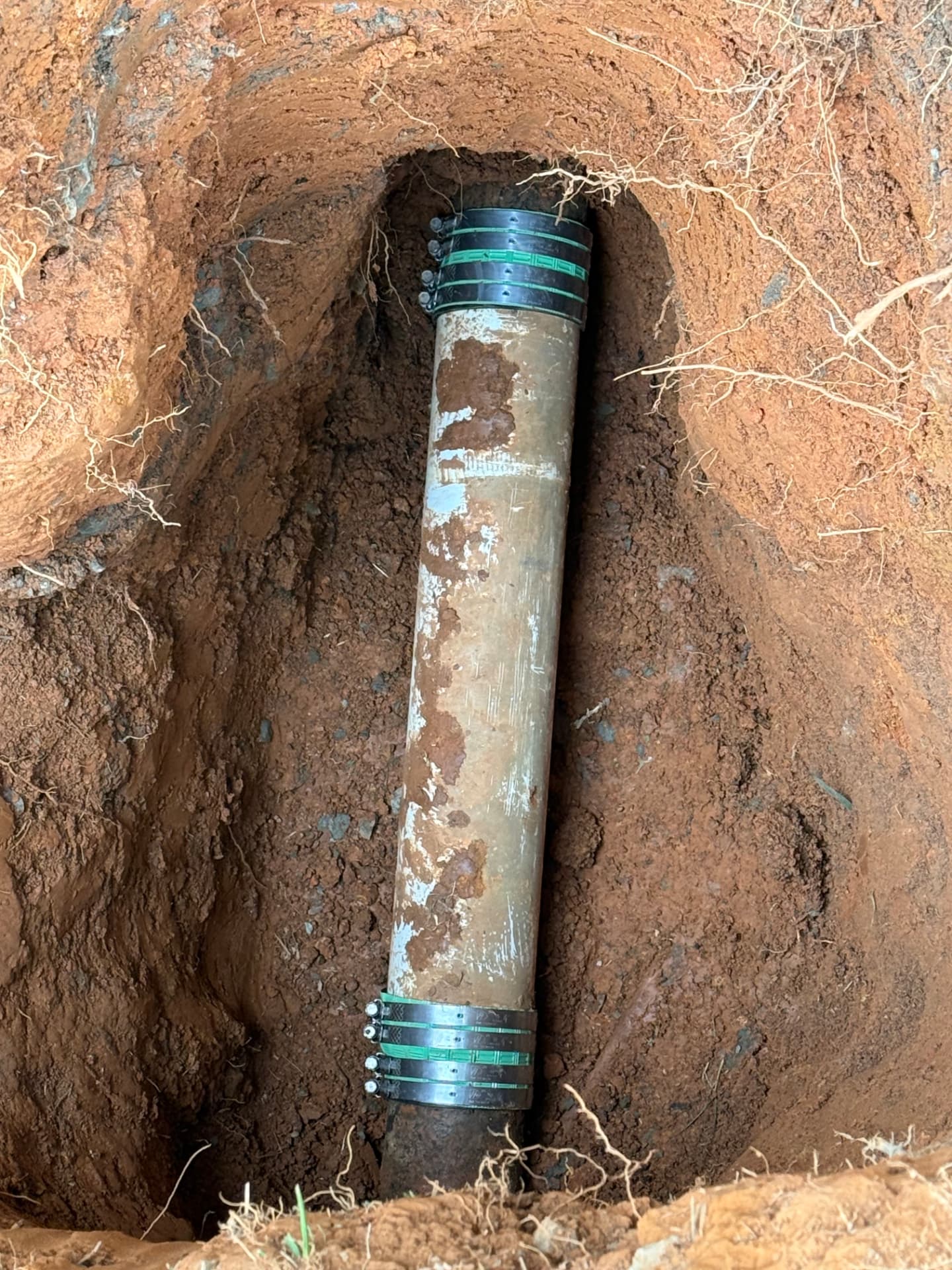 Buried pipe repaired with clamps in a trench